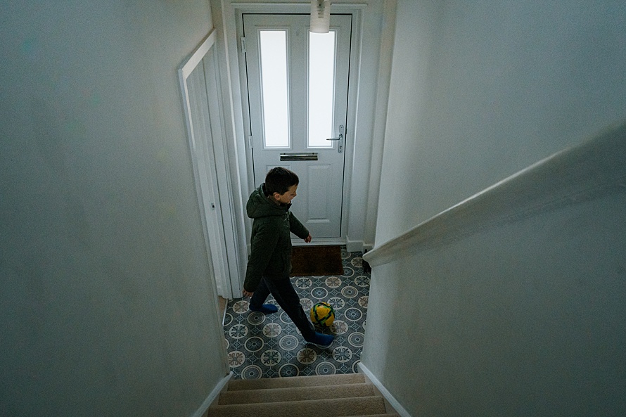 Boy kicking yellow football in house on family documentary photography session in Cambridge by Emma Collins