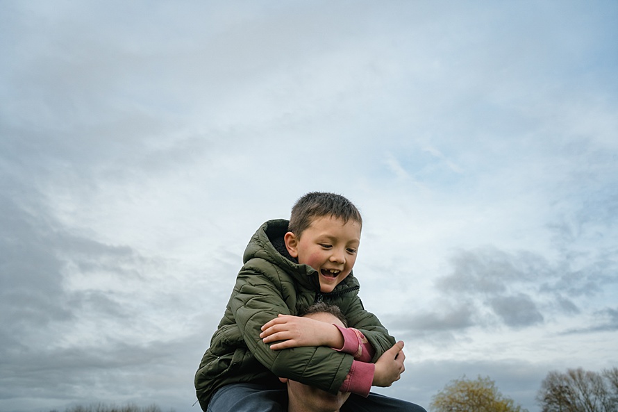 Cambridge family photographer captures unconventional shot of father giving his son a piggy back during a documentary family photoshoot