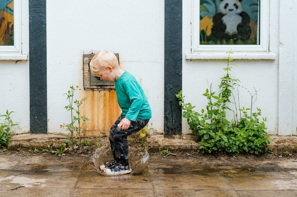 Little boy jumping in a puddle with a big splash, St Albans natural family photographer