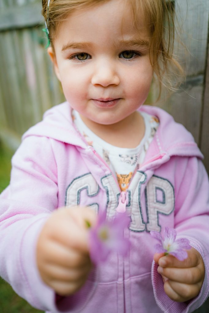 Portrait of little girl in pink holding a flower, candid nursery portraits in St Albans