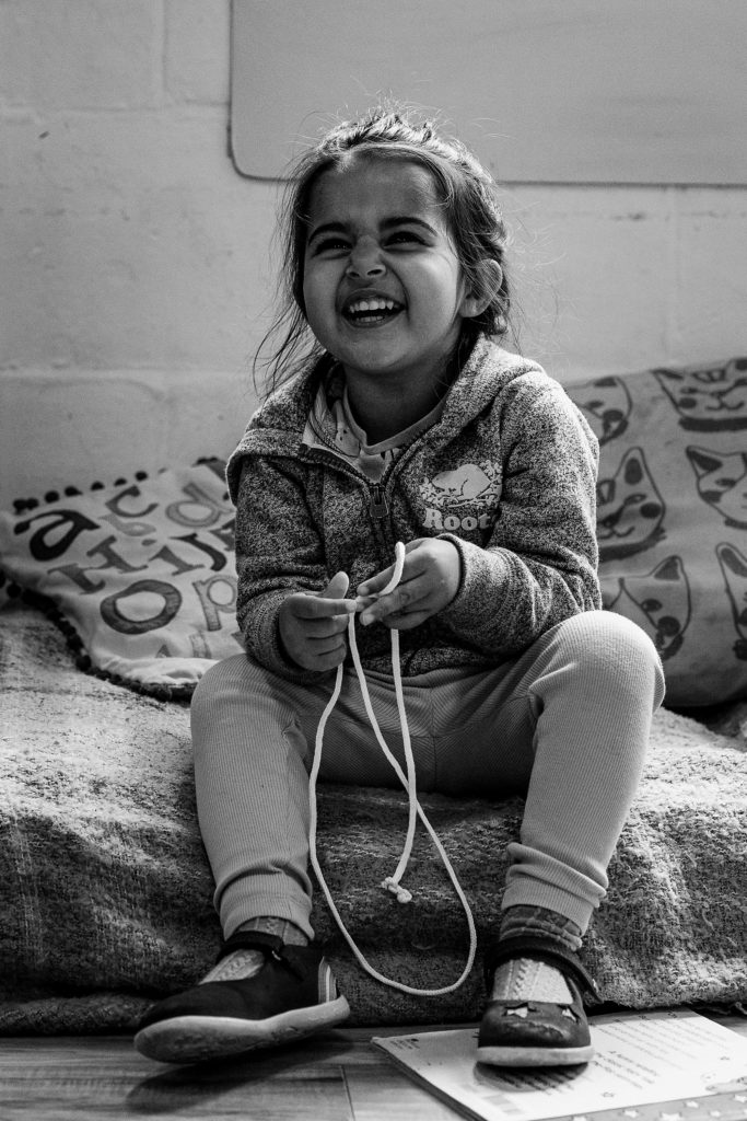Little girl playing with string and laughing, candid nursery portraits