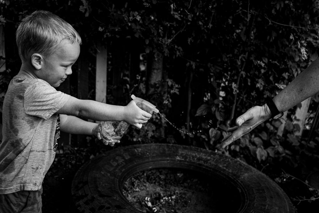 Little boy spraying someones hand with water, natural nursery photography