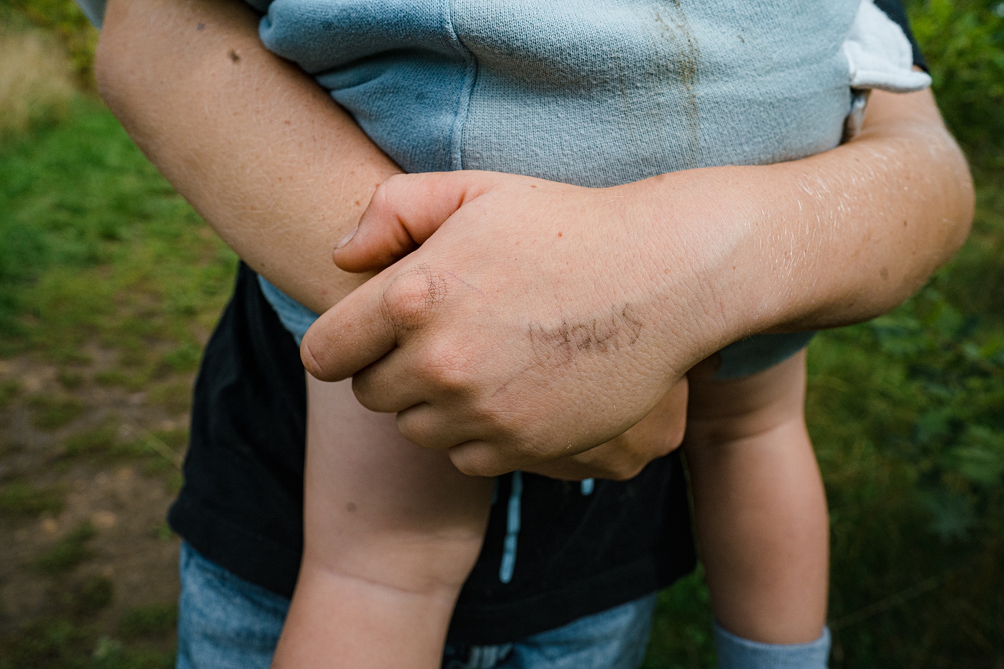 Boy carrying baby brother with pen on his hand, detail photo from a documentary family photoshoot